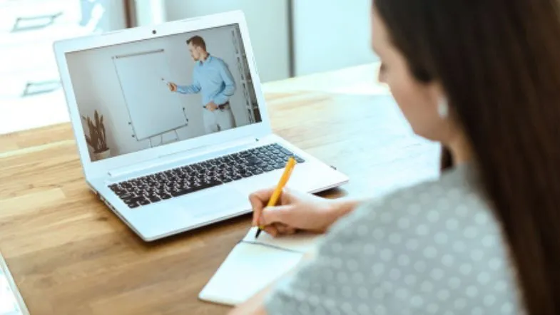Aluna assistindo aula virtual no notebook e fazendo anotações, representando o aprendizado dinâmico dos cursos EAD na área da saúde.