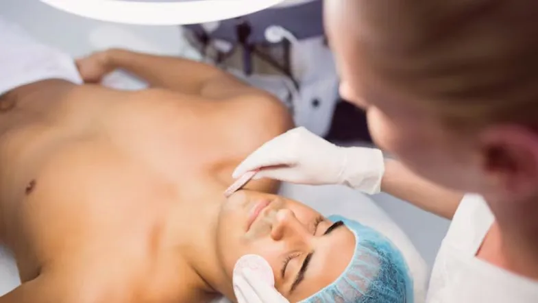 Principais procedimentos da estética avançada e como a pós-graduação prepara você 8 Tratamento facial em paciente masculino com profissional em estética avançada aplicando cuidados estéticos em clínica especializada.