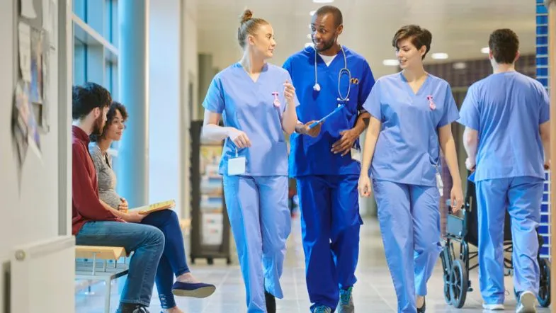 Comunicação ineficaz e a cultura do silêncio nas equipes de saúde: impactos e soluções 8 Equipe multiprofissional da saúde caminhando e conversando de forma leve em ambiente hospitalar.
