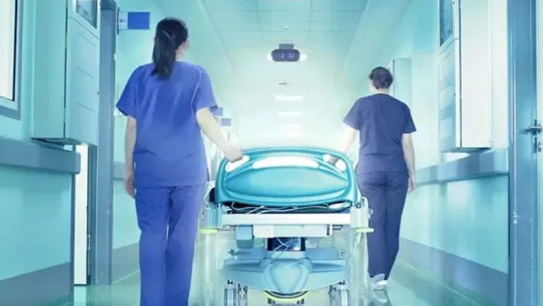 Equipe de enfermagem conduzindo maca por corredor de hospital em direção à unidade de terapia intensiva.