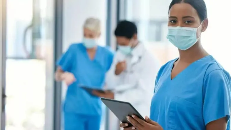 Comunicação ineficaz e a cultura do silêncio nas equipes de saúde: impactos e soluções 9 Enfermeira com tablet à frente, com outros profissionais ao fundo em hospital.
