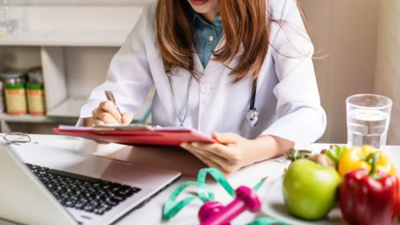 Evento Nutri Inteligente: acompanhe as tendências em nutrição clínica e esportiva 8 Nutricionista escrevendo prescrição alimentar em consultório com notebook e alimentos naturais