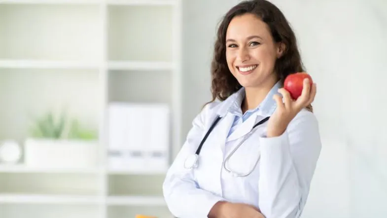 Nutricionista sorridente segura maçã vermelha, representando hábitos alimentares saudáveis e a importância da Nutrição na saúde.
