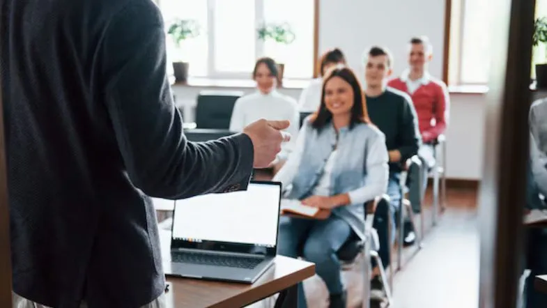 Novo marco regulatório da Educação a Distância: o que muda e quem será impactado 8 Professor ministrando aula presencial para turma de estudantes em sala com notebooks abertos.