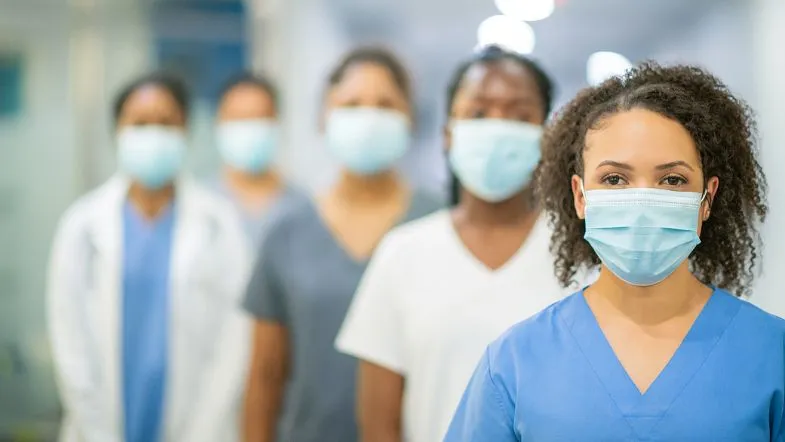 10 caminhos na pós-graduação para transformar sua carreira em Enfermagem 9 Grupo de profissionais da Enfermagem com máscaras cirúrgicas em corredor hospitalar, com destaque para a profissional à frente em foco.