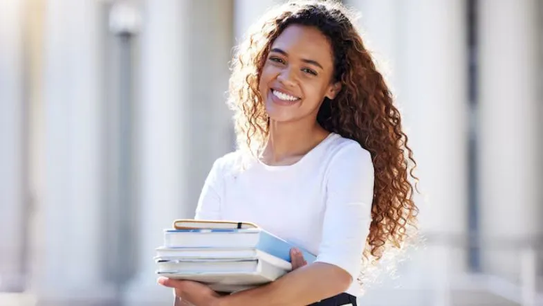 Como escolher o curso de graduação ideal para você: dicas práticas para decidir com segurança 9 Estudante sorridente segurando livros em frente ao campus, representando motivação e conquistas na graduação.