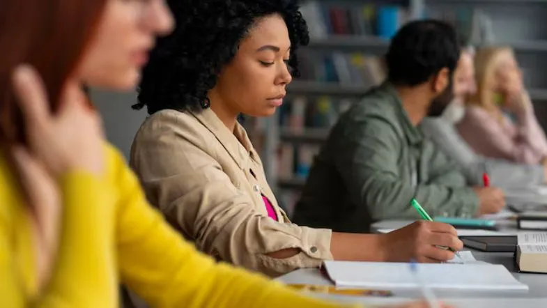 Alunos concentrados escrevendo em sala de aula durante atividades acadêmicas.