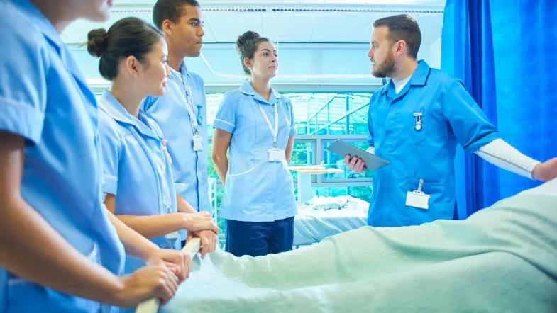 Grupo de estudantes de Enfermagem recebendo orientação prática em ambiente clínico.