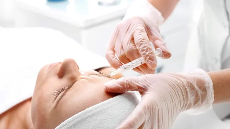 O que é Biomedicina Estética? Formação, regulamentação e áreas de atuação 11 Profissional aplicando toxina botulínica na testa de paciente com faixa branca, ilustrando prática comum na biomedicina estética.