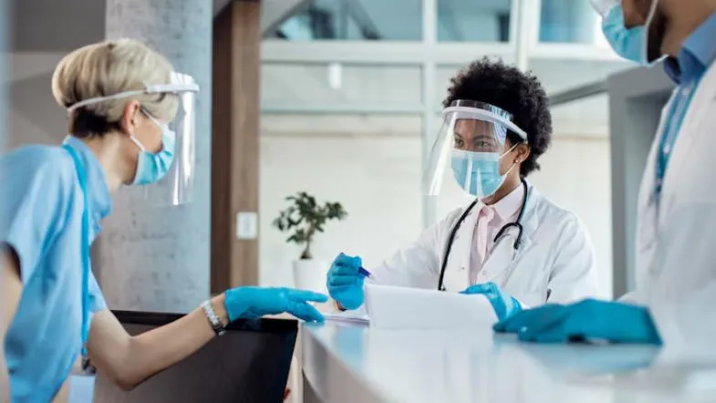 Segurança do paciente: como reduzir eventos adversos com protocolos simples 10 Equipe multiprofissional da saúde com equipamentos de proteção individual em reunião na recepção de hospital.