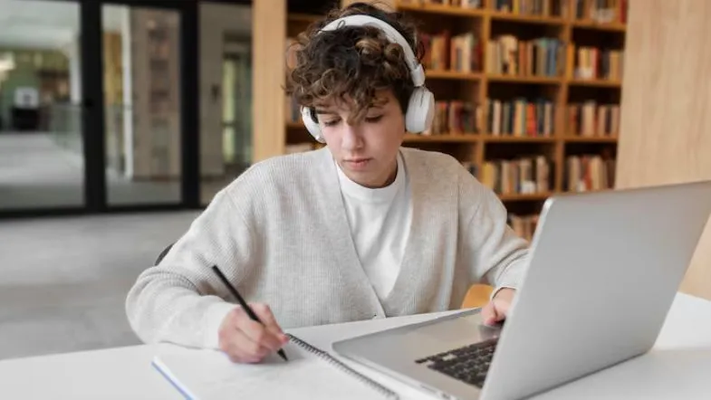 Edtech em Saúde: como o lifelong learning está transformando carreiras na saúde 11 Jovem com fones de ouvido estuda em frente ao notebook em biblioteca, representando o aprendizado por meio de plataformas edtech na área da saúde.