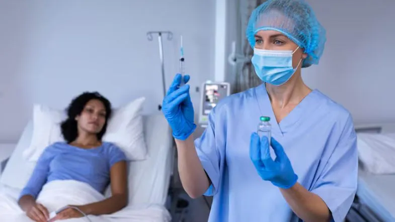 Enfermeira de UTI preparando seringa com medicação para paciente em ambiente hospitalar.