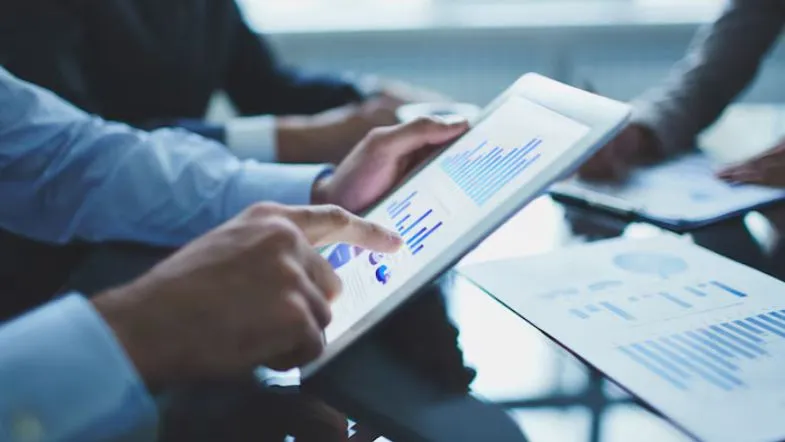 Profissional analisando gráficos e indicadores em tablet durante reunião de negócios.