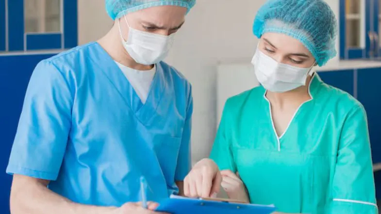 Dois profissionais de Enfermagem analisando prontuário em hospital.