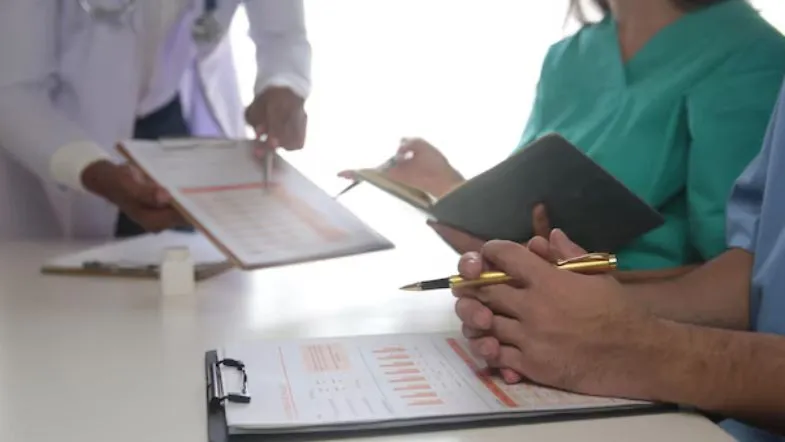 Equipe multiprofissional discutindo prontuários e indicadores de auditoria clínica.