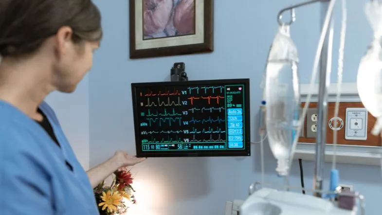 Enfermeira analisando monitor multiparamétrico em ambiente hospitalar durante atividade prática.