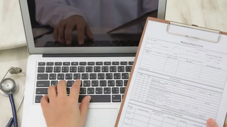 Auditoria hospitalar: como prevenir desperdícios e melhorar indicadores em saúde 11 Pessoa com prontuário médico em prancheta e notebook aberto, simbolizando o cruzamento de dados em auditoria de contas médicas.