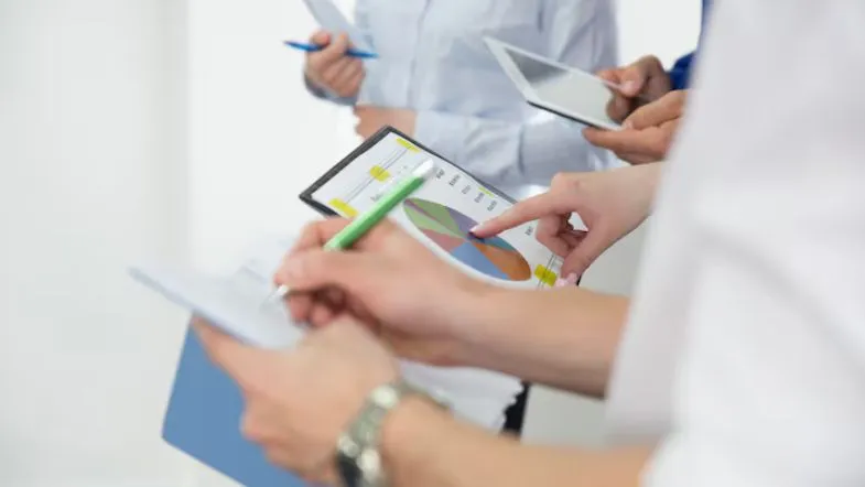 Profissionais analisando gráficos coloridos em relatórios e tablet durante reunião de gestão.