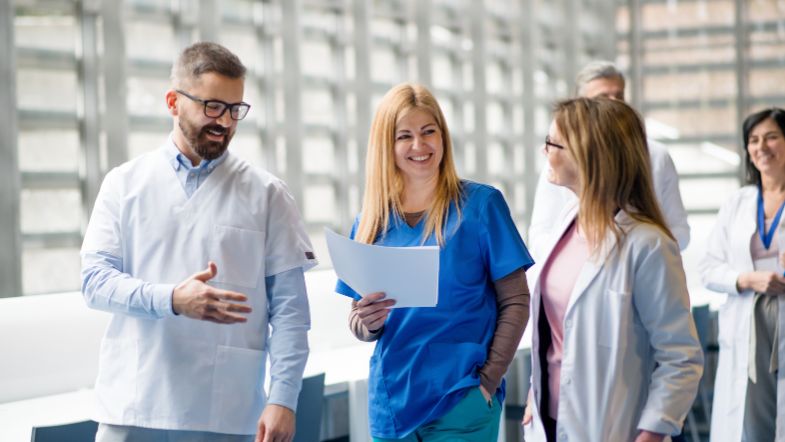 Equipe multiprofissional de saúde discutindo documentos, simbolizando trabalho colaborativo e melhoria contínua.