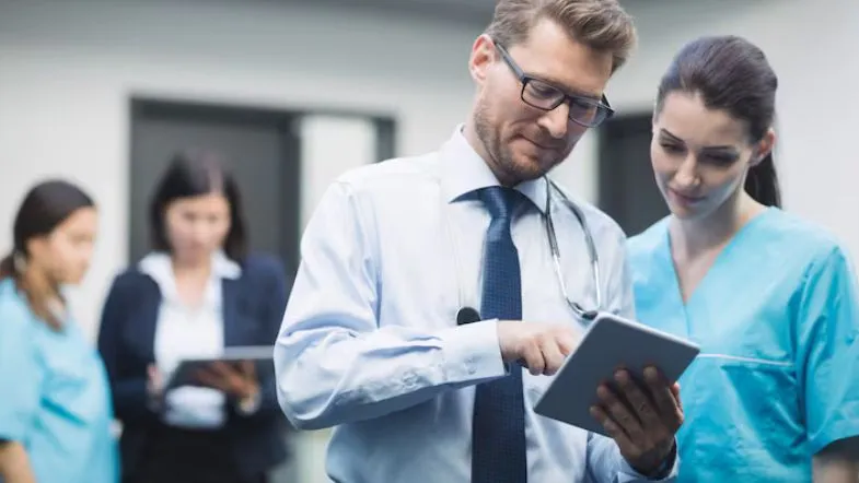 Médico e enfermeira utilizando tablet para revisar protocolos de auditoria em saúde.
