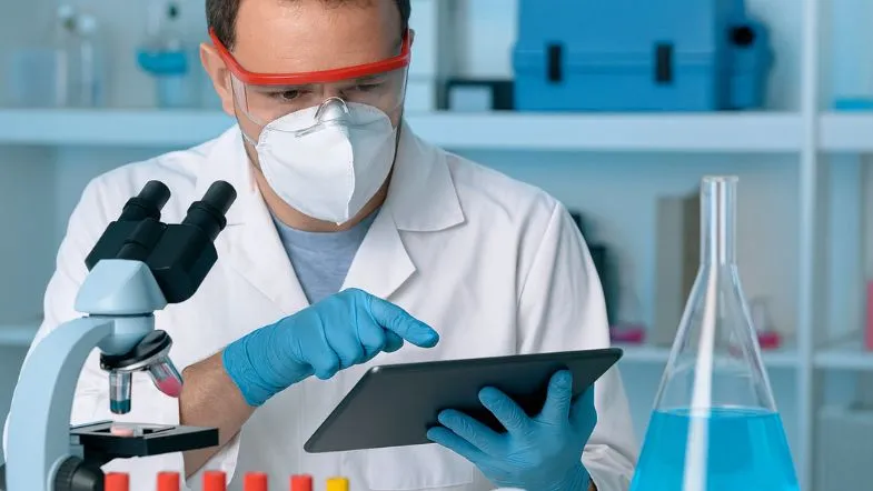 Biomédico com máscara de proteção usando tablet em laboratório com reagentes químicos.