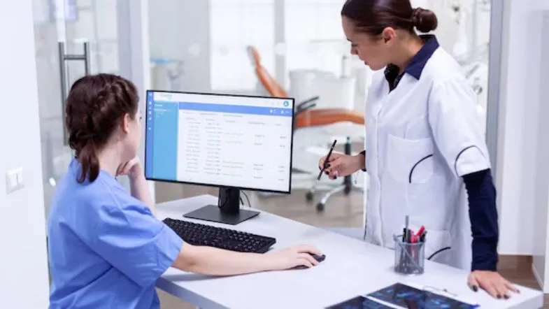 Auditoria hospitalar: como prevenir desperdícios e melhorar indicadores em saúde 12 Duas profissionais da saúde analisando dados em tela de computador, representando a auditoria hospitalar com foco em indicadores e performance.