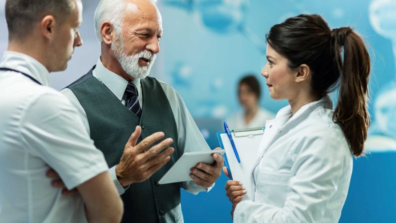 Profissional sênior discutindo protocolos com médicos, simbolizando liderança e auditoria em saúde.