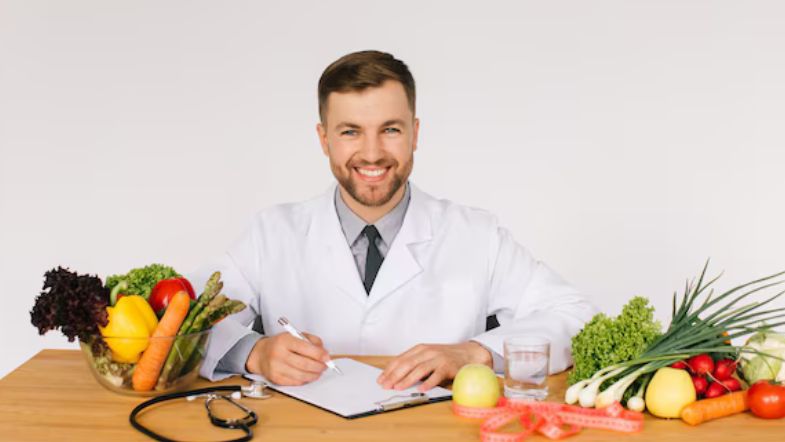 Nutricionista sorridente em consultório com mesa cheia de frutas, vegetais e instrumentos clínicos.