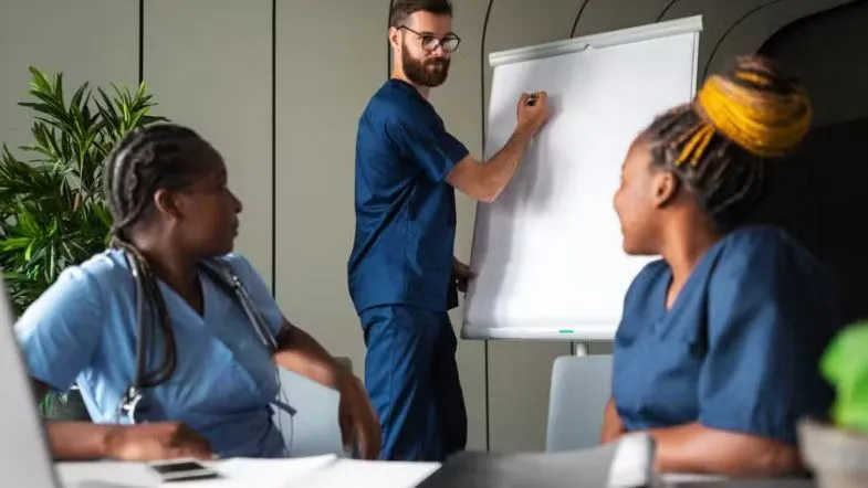 Inteligência emocional na liderança: diferencial que transforma profissionais em referência 6 Equipe de profissionais da saúde em discussão diante de quadro branco, durante reunião de equipe.