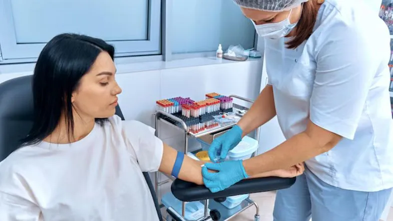 Enfermeira realizando coleta de sangue em paciente com luvas e máscara, aplicando protocolos de biossegurança e qualidade laboratorial.