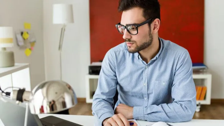 Jovem estudante de Recursos Humanos concentrado em estudos no computador em ambiente de trabalho moderno.