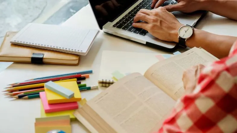 Mesa de estudos com laptop, livros e post-its coloridos, mostrando métodos de organização para preparação do ENEM 2025.