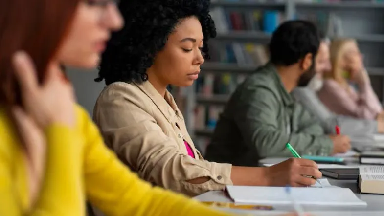 Alunos de Recursos Humanos estudando em biblioteca, com foco em anotações e leitura de materiais acadêmicos.