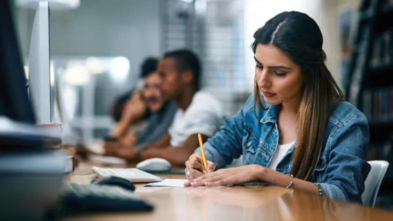 Como escolher a graduação certa: 7 passos para evitar frustrações 7 Jovem concentrada estuda em biblioteca para decidir o curso ideal e planejar sua trajetória acadêmica.