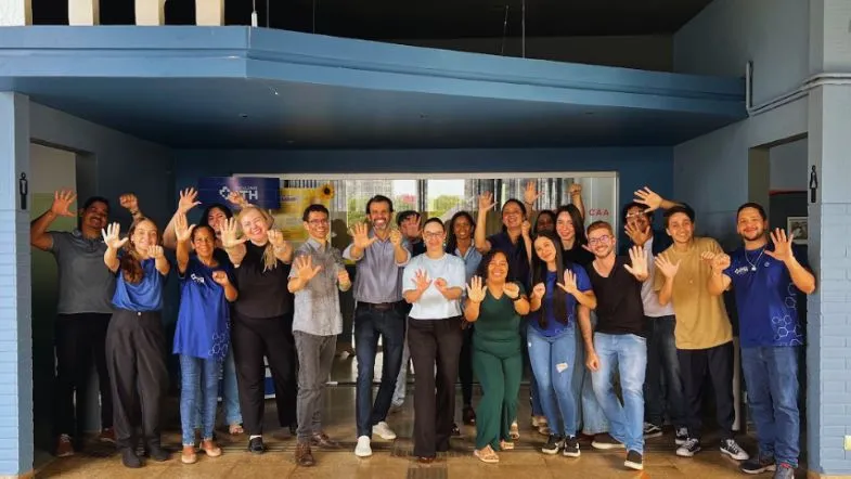 Colaboradores da Faculdade ITH posando sorridentes na entrada da instituição em Goiânia.