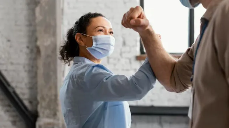 Profissional da saúde cumprimentando colega com cotovelo, simbolizando ética, respeito e trabalho colaborativo.
