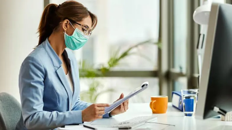 Auditoria, acreditação e compliance na saúde: os novos pilares da saúde em 2025 9 Gestora hospitalar com máscara revisa documentos de compliance e acreditação em ambiente corporativo de saúde.