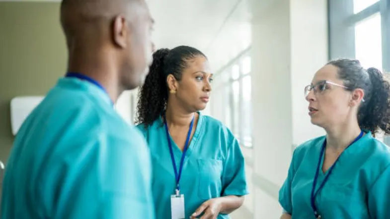 Inteligência emocional na liderança: diferencial que transforma profissionais em referência 9 Grupo de profissionais de enfermagem dialogando em corredor de hospital, simbolizando empatia e escuta ativa na liderança.