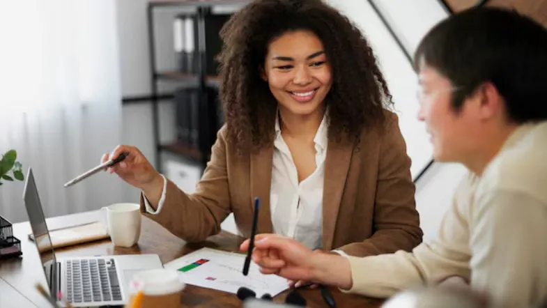 Dois profissionais de Recursos Humanos em reunião, sorrindo enquanto discutem planos de desenvolvimento de pessoas.