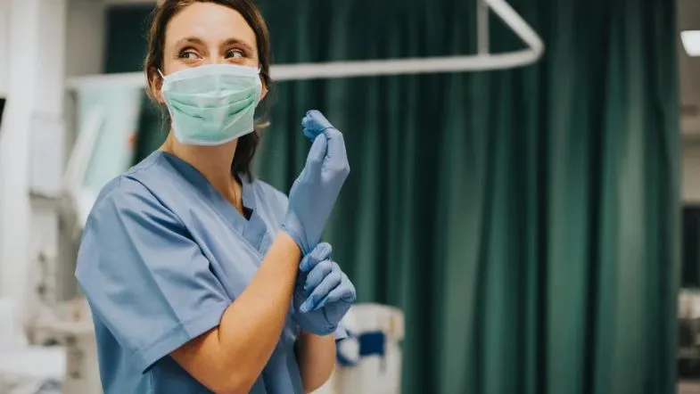 Enfermeira com máscara e luvas em ambiente hospitalar, simbolizando ética, cuidado e responsabilidade na atuação profissional.