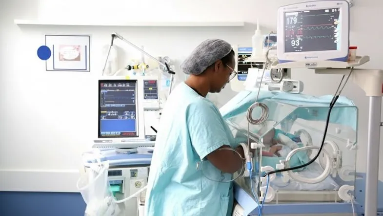Quanto dura a pós em UTI Neonatal e Pediátrica? Entenda a duração ideal 6 Enfermeiro verificando parâmetros e cuidando de recém-nascido em incubadora dentro de uma UTI Neonatal equipada.