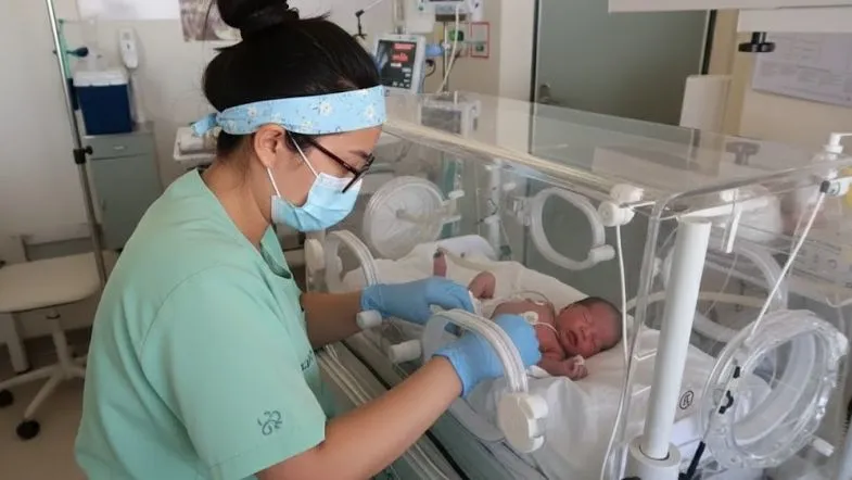 Apgar, reanimação e ventilação: o guia completo da prática em UTI Neonatal e Pediátrica em 2025 6 Profissional de saúde usando máscara e luvas enquanto manipula uma incubadora com recém-nascido.