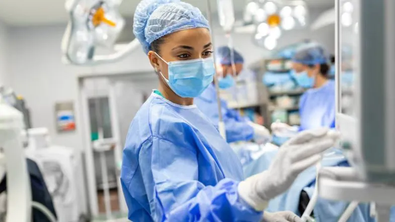 Enfermeira intensivista ajustando monitor multiparamétrico dentro de uma unidade de terapia intensiva.