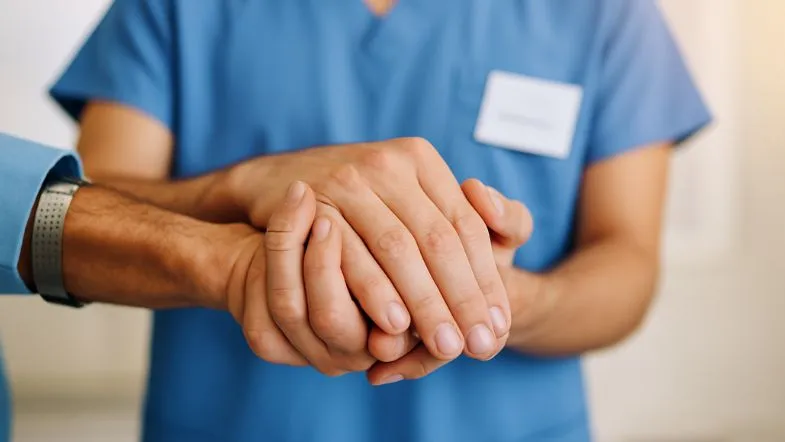 Profissional de saúde segurando as mãos de um paciente em gesto de acolhimento e cuidado, ato necessário para quem trabalha com a saúde pública.
