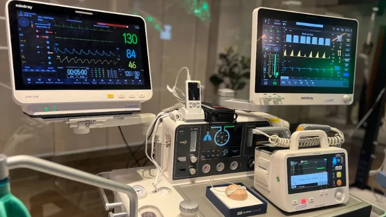 Monitores multiparamétricos e equipamentos avançados de suporte à vida posicionados em bancada de laboratório de simulação clínica.