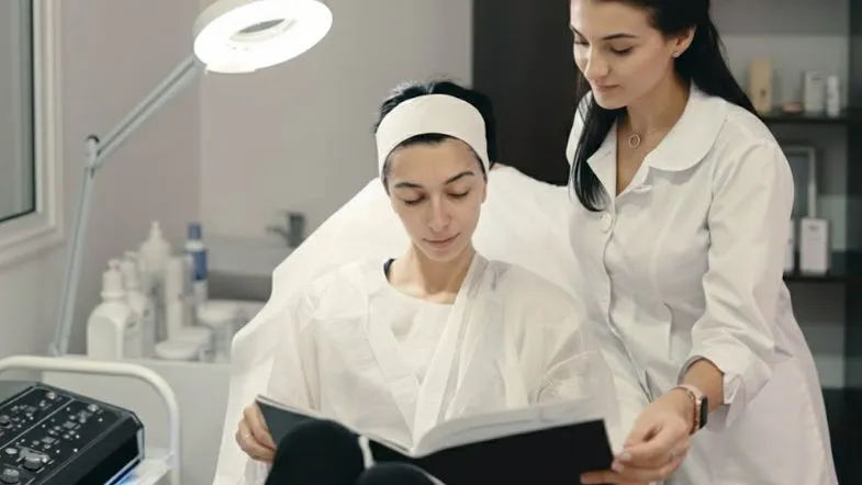 Profissional explicando procedimento estético para paciente que consulta um material informativo durante o atendimento.