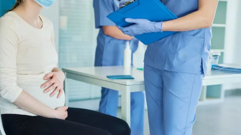 Enfermeiro obstetra anotando informações clínicas enquanto gestante aguarda avaliação no consultório.