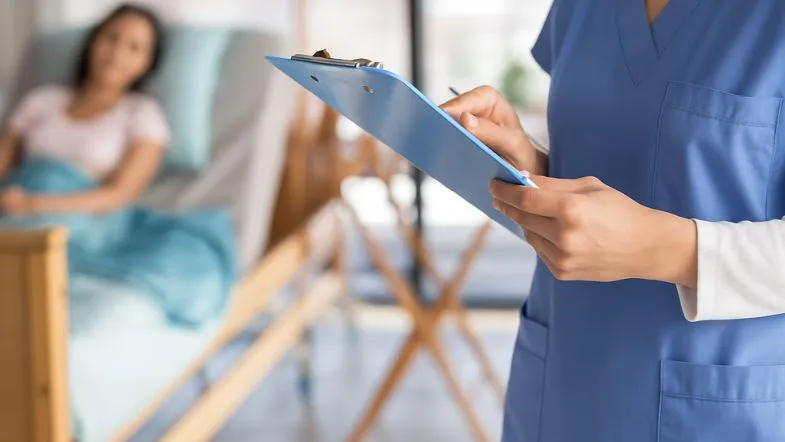 Câncer pode crescer 75% até 2050: como isso impacta a urgência e emergência? 7 Profissional de enfermagem registrando informações no prontuário enquanto paciente oncológica repousa no leito hospitalar.