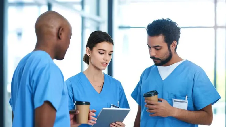 Três profissionais de saúde conversando e analisando informações em ambiente clínico, reforçando o trabalho em equipe.