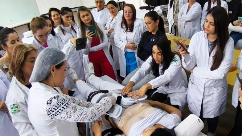 Grupo de alunos observando procedimento corporal em aula prática dentro de clínica escola.